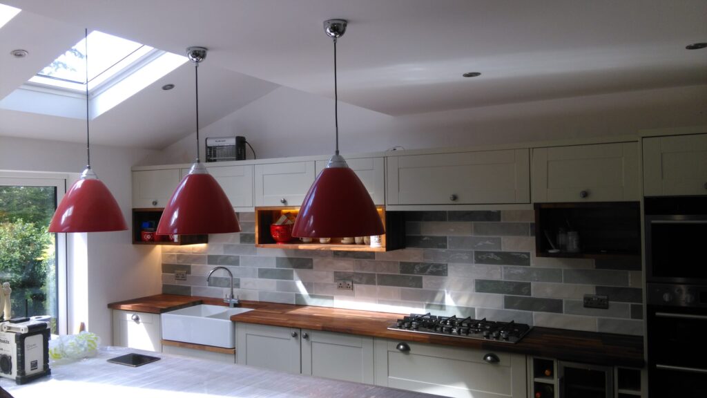 Modern kitchen with red pendant lamps, featuring a stainless steel sink and gas stove, showcasing AMBS Eco Solutions' style.