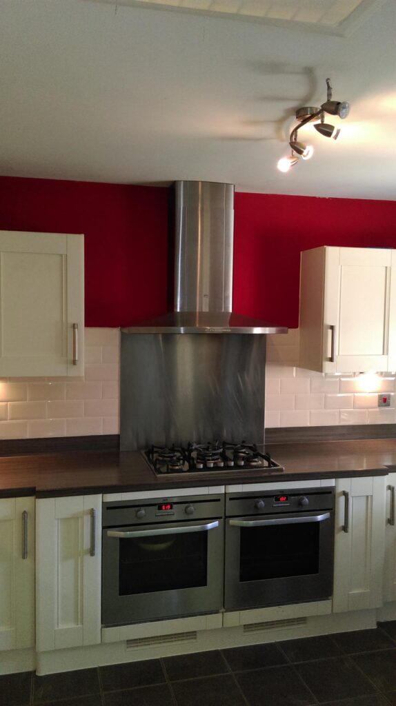 Modern kitchen with stainless steel appliances, gas stovetop, red accents, and inviting design. AMBS Eco Solutions.