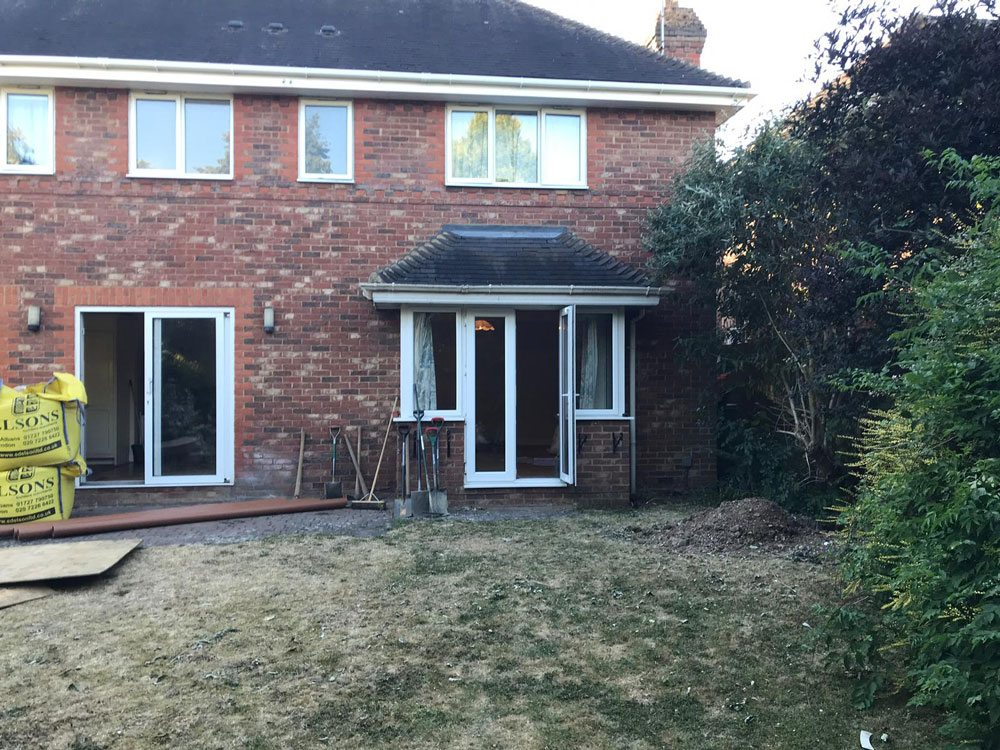 Red brick house under renovation with construction supplies, showcasing AMBS Eco Solutions' building services.